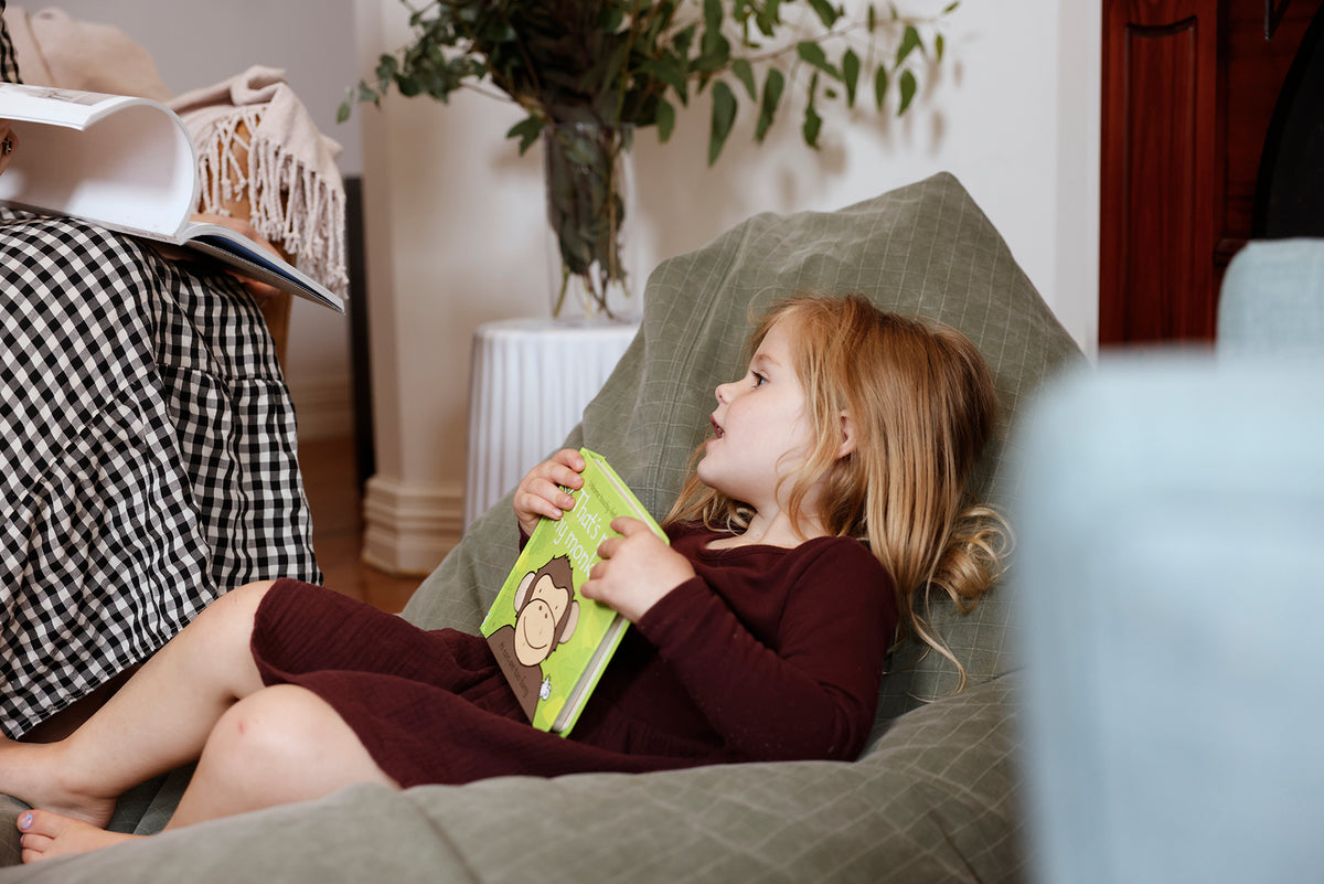 A girl holding a book in a sage-green bean bag