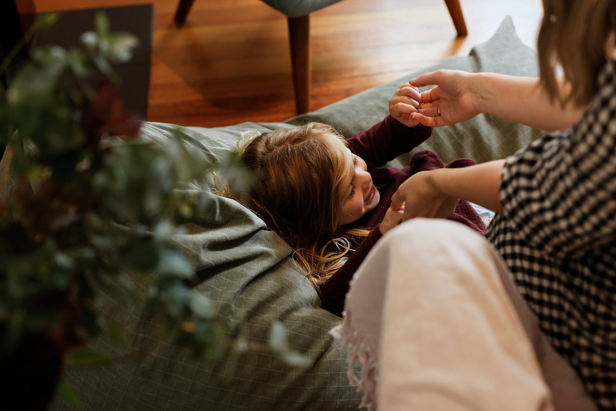 Child lying on a green bean bag, holding a parent's hand