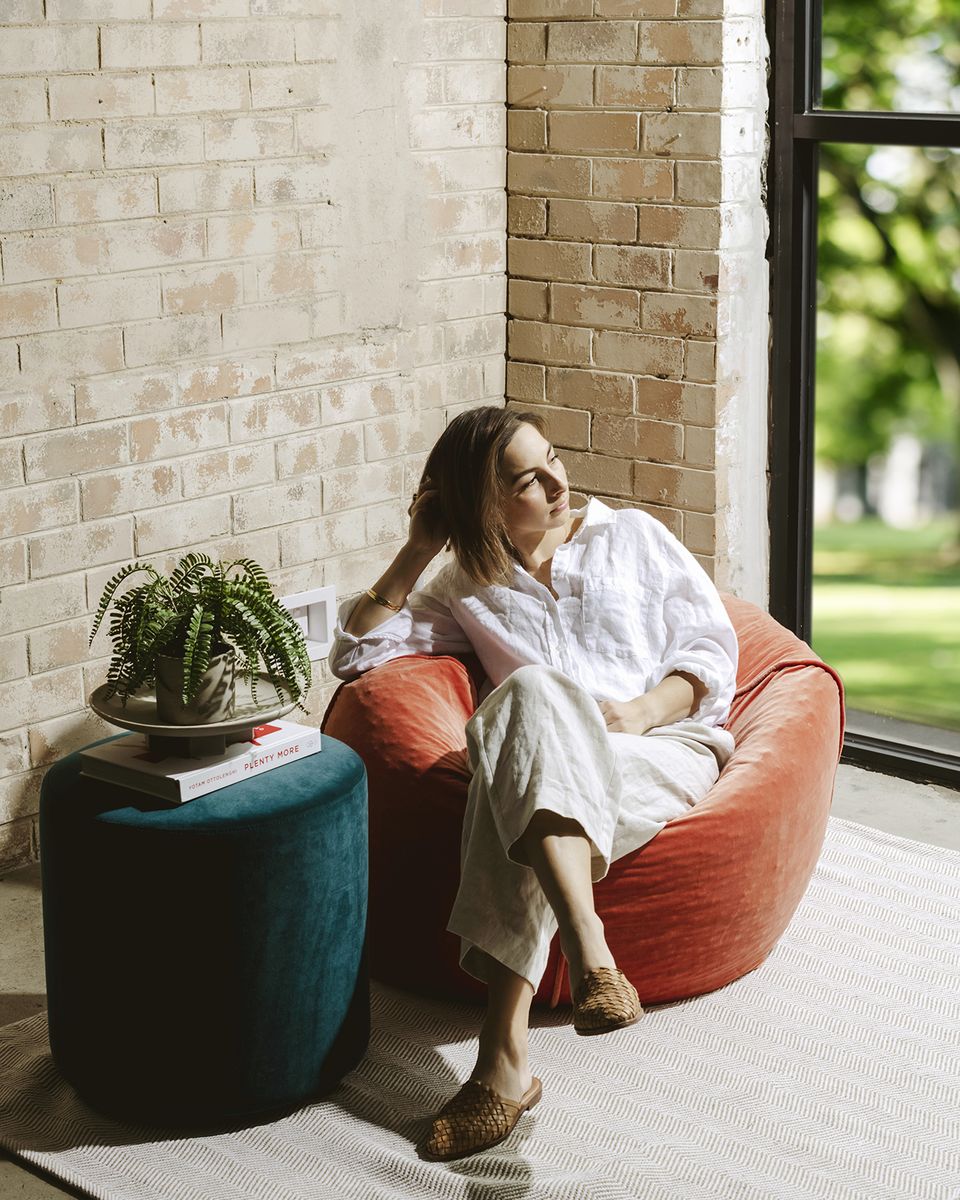 Woman relaxing on a red bean bag by a window
